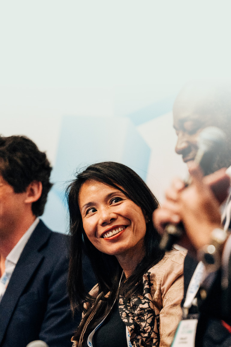 Vivian Wu smiles while seated on a panel and looking towards another speaker.