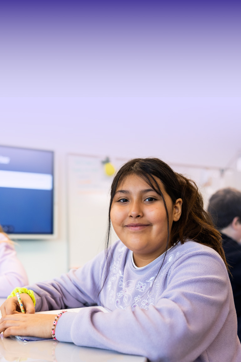 Girl in purple sweater smiles in classroom with other students